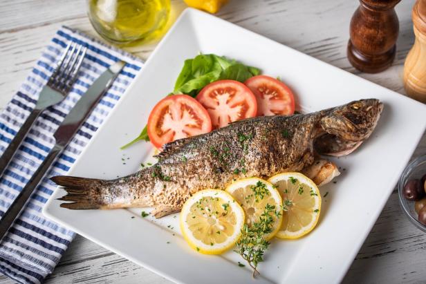 Ein gegrillter Fisch wird mit Zitronen- und Tomatenscheiben auf einem Teller serviert.