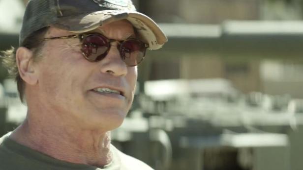 Arnold Schwarzenegger mit Sonnenbrille und Kappe im Gespräch.