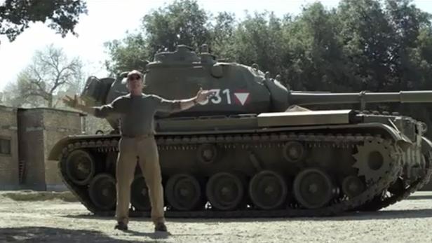 Ein Mann steht mit ausgestreckten Armen vor einem Panzer.