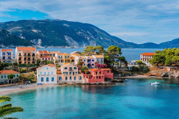 Blick auf die bunten Häuser von Assos auf Kefalonia, Griechenland, mit dem Ionischen Meer im Vordergrund.