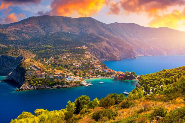 Blick auf Assos, Kefalonia, mit bunten Häusern an einer Bucht und Bergen im Hintergrund.