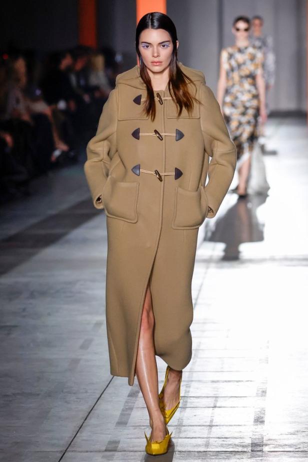 Kendall Jenner läuft in einem langen, beigen Dufflecoat und gelben Schuhen über den Laufsteg.