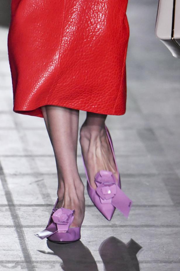Nahaufnahme von den Füßen eines Models mit lila Schuhen und einem roten Rock.