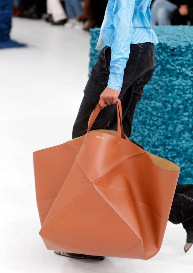 Eine Person trägt eine übergroße, braune Ledertasche von Loewe.