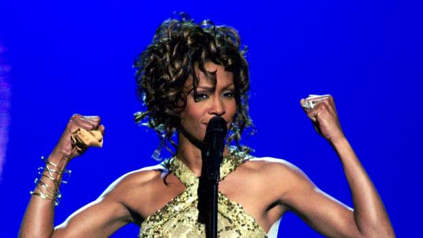 Whitney Houston singt mit erhobenen Fäusten auf der Bühne.