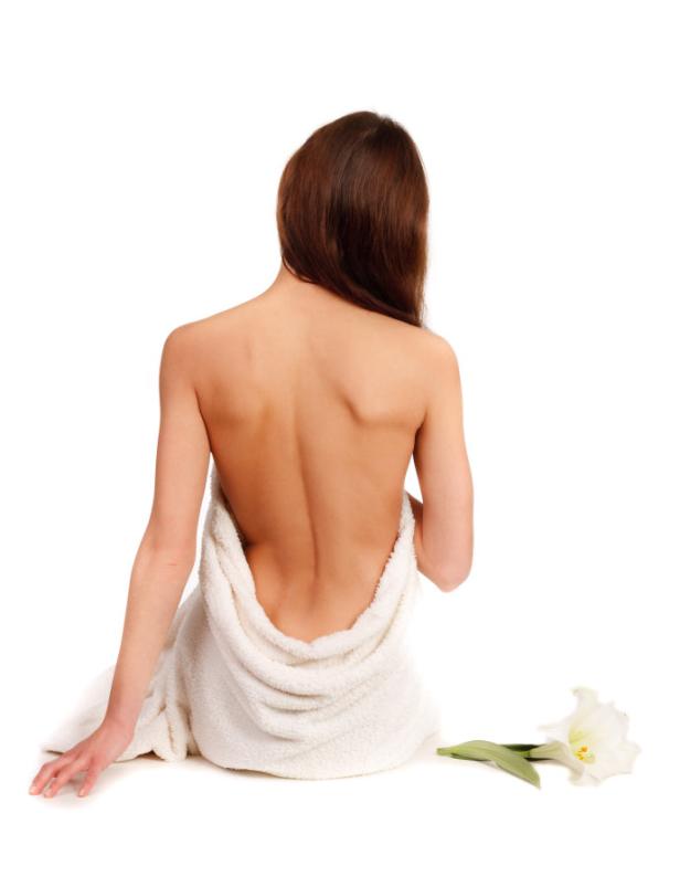 Eine Frau mit einem Handtuch sitzt mit dem Rücken zum Betrachter neben einer Lilie.