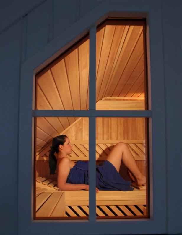 Eine Frau entspannt eingewickelt in ein blaues Tuch in einer Sauna.