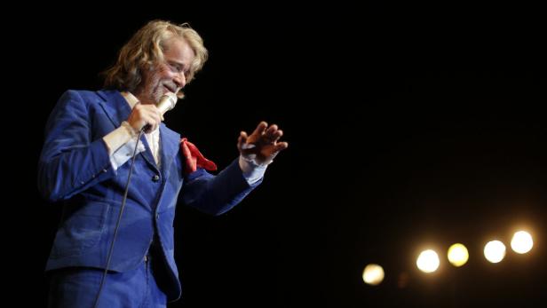 Ein Mann mit langem blonden Haar singt in einem blauen Anzug ins Mikrofon.