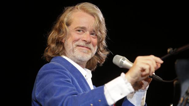Ein Mann mit langen blonden Haaren hält ein Mikrofon in der Hand.