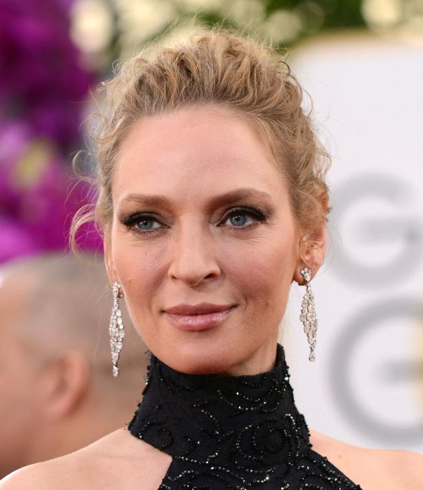 Uma Thurman mit hochgesteckten blonden Haaren und langen Diamantohrringen.