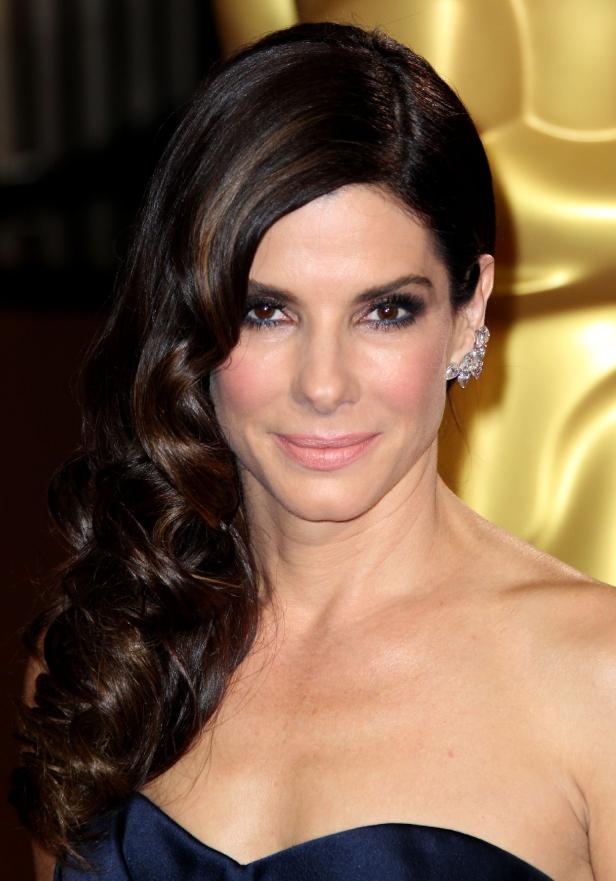 Sandra Bullock posiert auf einem roten Teppich mit einem eleganten, dunklen Kleid.