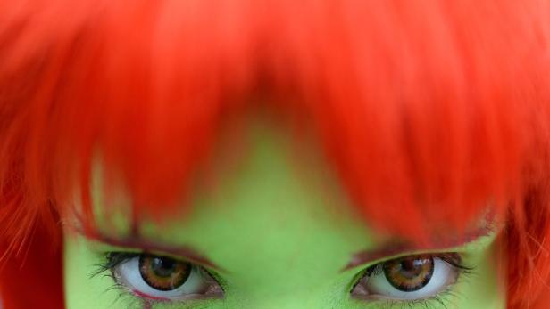 Nahaufnahme des Gesichts einer Frau mit grüner Haut und roter Perücke.