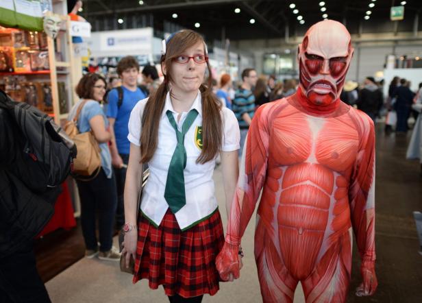 Eine junge Frau im Schulmädchen-Cosplay hält Händchen mit jemandem im Kostüm eines Titanen aus „Attack on Titan“.