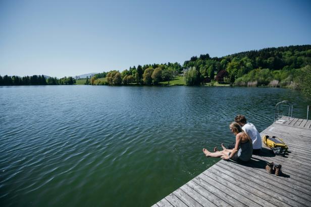 Ein Paar sitzt auf einem Holzsteg am Maltschacher See in Kärnten.