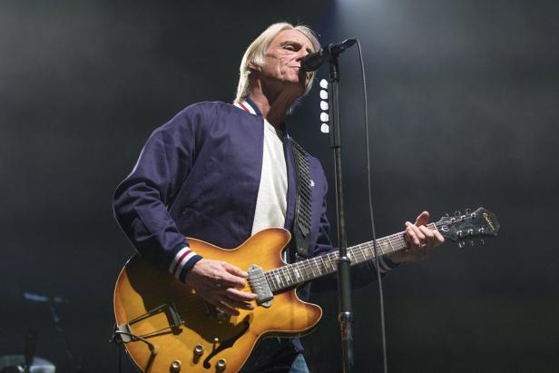 Paul Weller spielt Gitarre und singt während eines Konzerts.