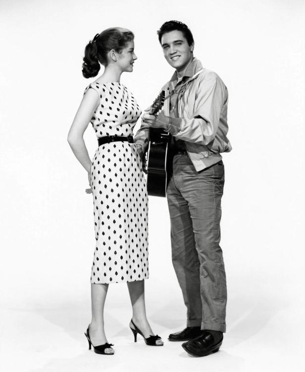 Elvis Presley mit Gitarre und eine junge Frau in einem gepunkteten Kleid stehen zusammen.