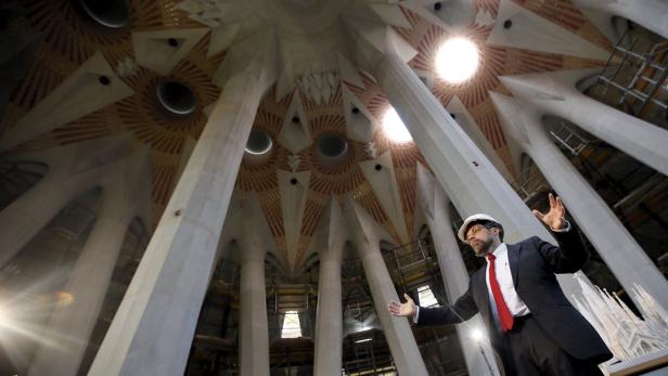 Ein Mann mit Schutzhelm steht im Inneren der Sagrada Familia und deutet auf die Decke.