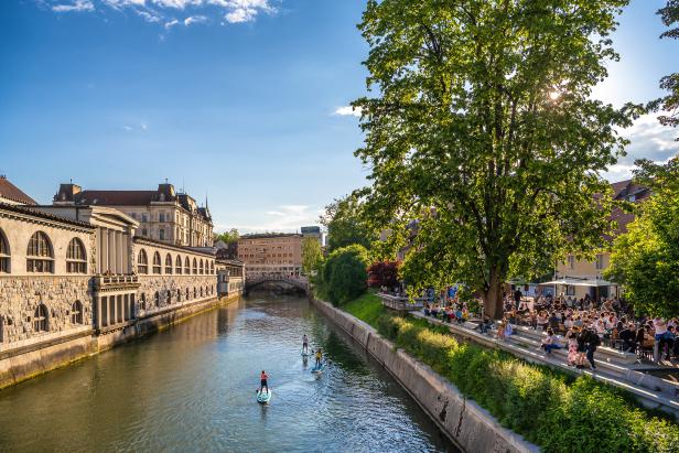 Die Ljubljanica fließt durch Ljubljana, während Menschen auf dem Fluss Stand-Up-Paddling betreiben.