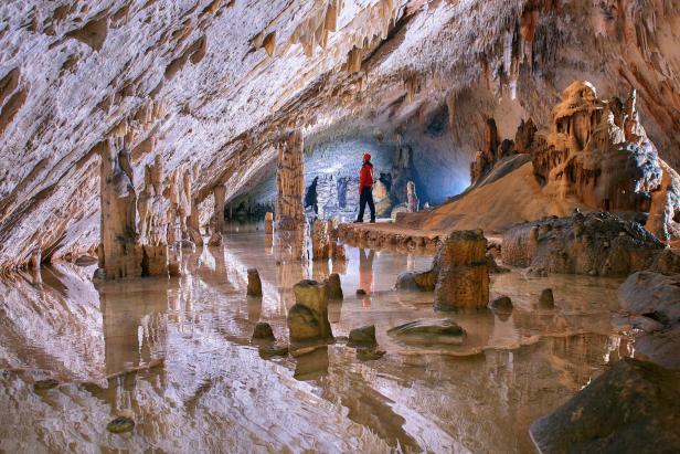 Eine Person steht in einer Höhle mit Stalaktiten und Wasserbecken.