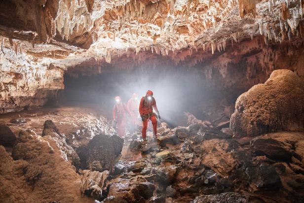 Eine Gruppe von Höhlenforschern in roter Schutzkleidung erkundet eine Höhle mit Stalaktiten.
