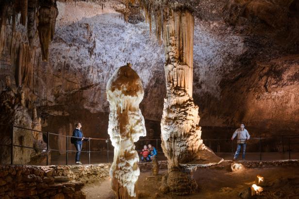 Besucher bewundern die Stalaktiten und Stalagmiten in einer beleuchteten Höhle.