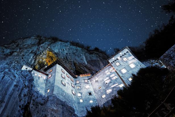 Burg Predjama, eine Höhlenburg in Slowenien, bei Nacht unter einem Sternenhimmel.