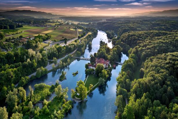 Luftaufnahme von Schloss Otočec auf einer Insel in der Krka, umgeben von Wäldern.
