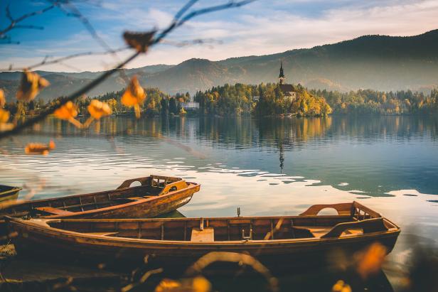 Zwei Holzboote liegen am Ufer des Bleder Sees mit Blick auf die Kirche auf der Insel.