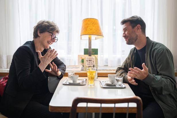 Zwei Personen sitzen an einem Tisch in einem Café und unterhalten sich angeregt.