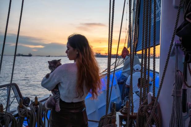 Eine Frau hält eine Katze auf einem Segelboot bei Sonnenuntergang.