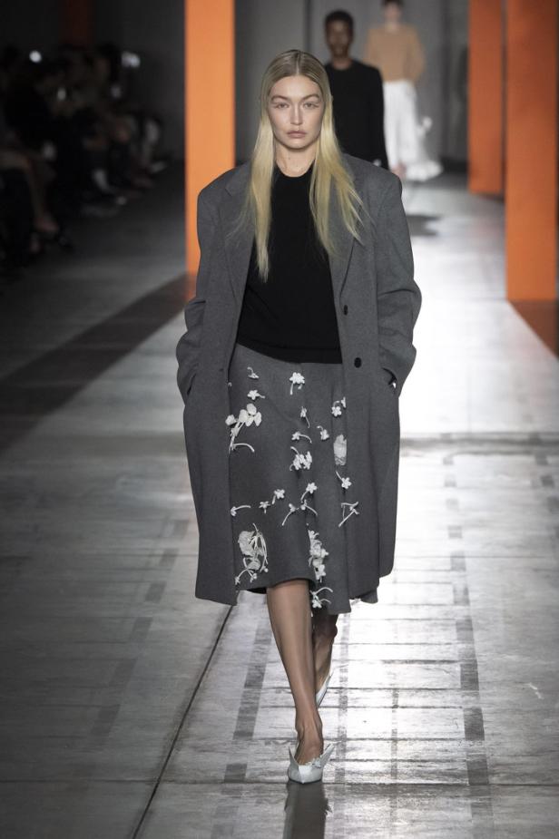 Gigi Hadid läuft in einem grauen Mantel und Rock mit Blumenmuster über einen Laufsteg.