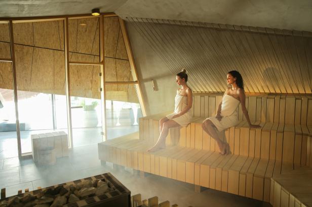 Zwei Frauen sitzen in Handtücher gehüllt in einer Sauna.