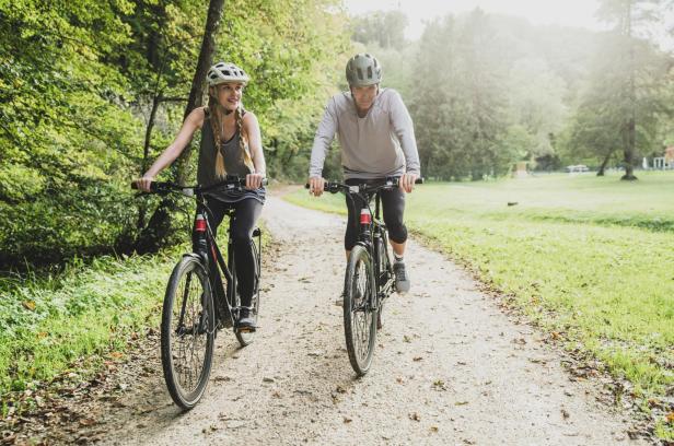 Ein Mann und eine Frau fahren mit Fahrrädern auf einem Weg durch den Wald.