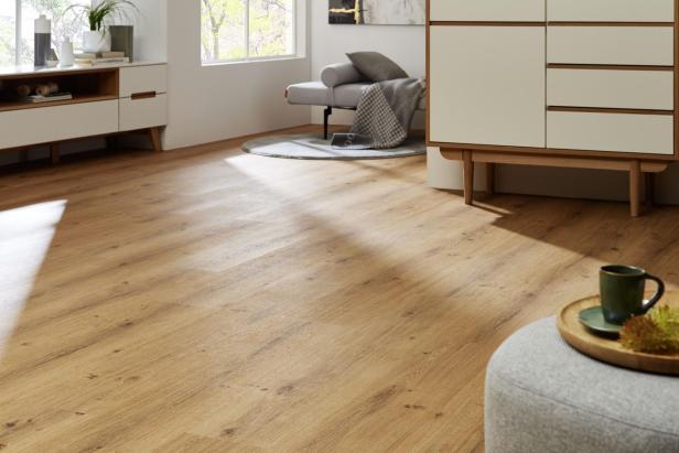 Heller Raum mit Holzfußboden, modernen weißen Möbeln, einem grauen Sessel und einem Tablett mit Tasse auf einem Hocker.