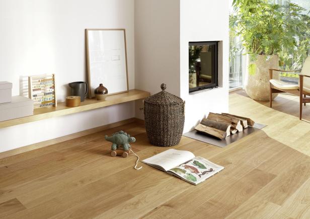 Helles Wohnzimmer mit Holzboden, Spielzeug-Dinosaurier, offenem Buch, Kamin, Holzscheiten und großen Pflanzen.