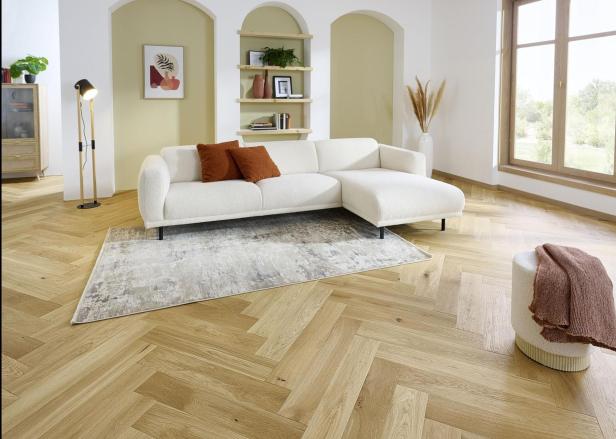 Ein Wohnzimmer mit Fischgrätenparkett, einem weißen Sofa und einem Fenster.