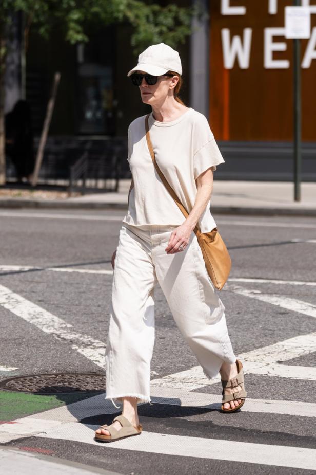 Eine Frau mit Sonnenbrille und Kappe überquert eine Straße.