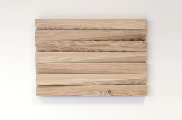 Mehrere helle Holzbretter sind horizontal an einer weißen Wand angebracht.
