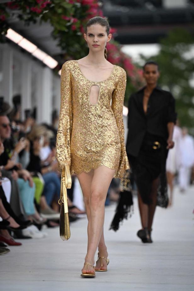 Ein Model präsentiert ein goldenes Paillettenkleid mit langen Ärmeln auf dem Laufsteg.