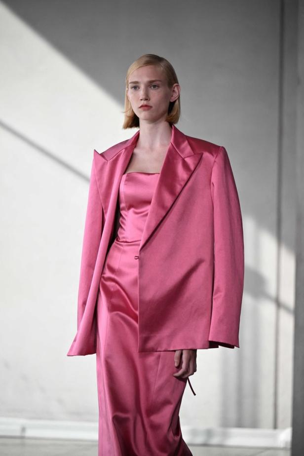 Eine Frau präsentiert ein pinkfarbenes Ensemble aus Blazer, Top und Rock.
