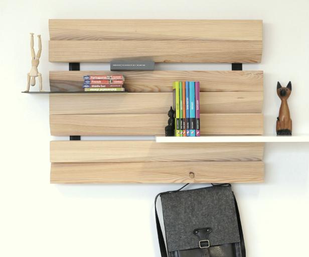 Ein Holzregal an einer weißen Wand mit Büchern, einer Holzfigur und einer Tasche.