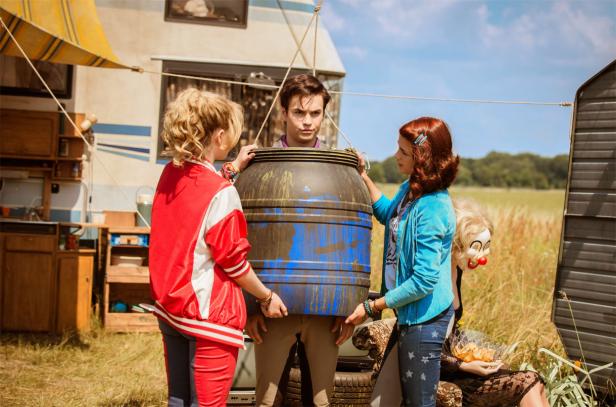 Drei Jugendliche hantieren mit einer blauen Tonne vor einem Wohnwagen.