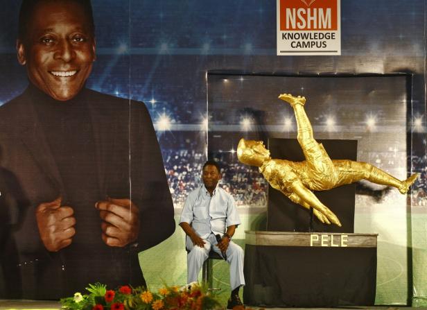 Ein Mann sitzt vor einem Hintergrund mit einem Porträt und einer goldenen Statue von Pelé.