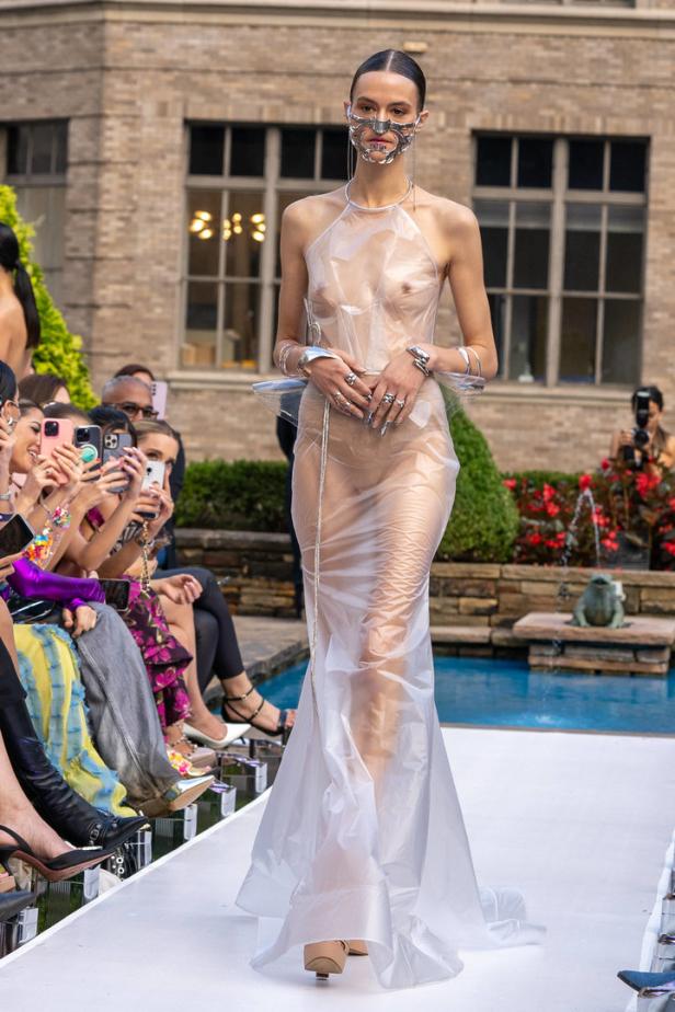 Eine Frau mit einer silbernen Maske und einem transparenten Kleid läuft über einen Laufsteg.