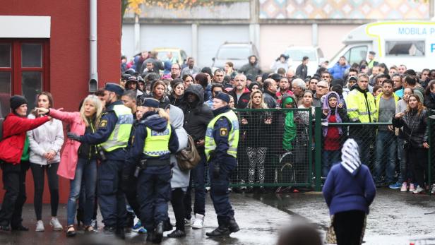 Eine Menschenmenge steht hinter einer Absperrung, bewacht von Polizisten.