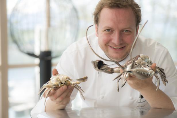 Ein lächelnder Koch präsentiert zwei kunstvolle Krabben aus Metall.