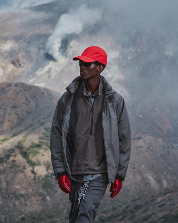 Ein Mann mit roter Kappe und Handschuhen steht vor einer vulkanischen Landschaft.