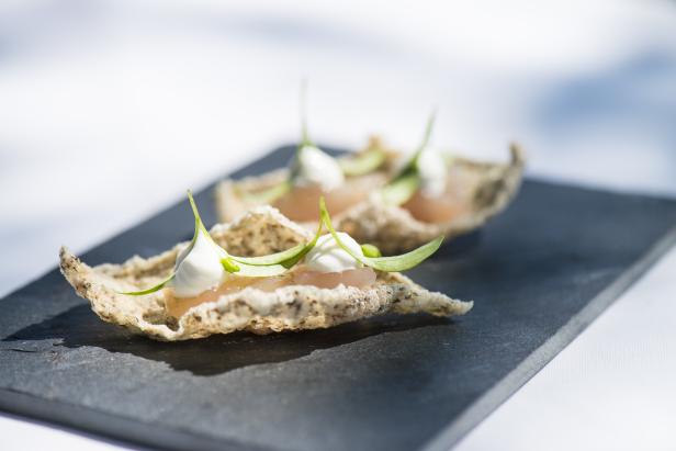 Zwei Canapés mit Creme, Fisch und Kräutern auf einem schwarzen Teller.