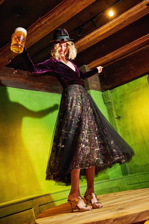 Eine Frau im Dirndl-Stil hält ein Bierglas in die Höhe.