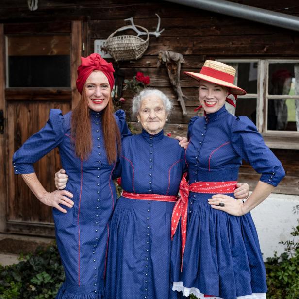 Drei Frauen in Trachten stehen vor einem Holzhaus.